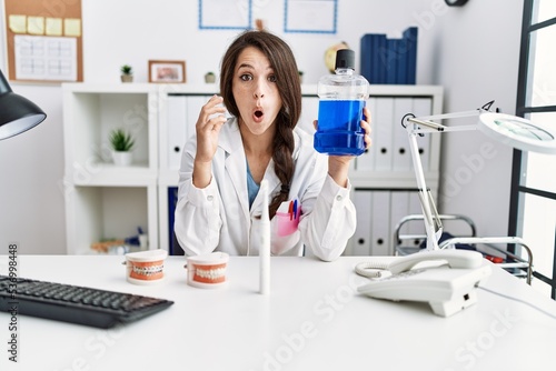 Young dentist woman holding mouthwash for fresh breath scared and amazed with open mouth for surprise, disbelief face