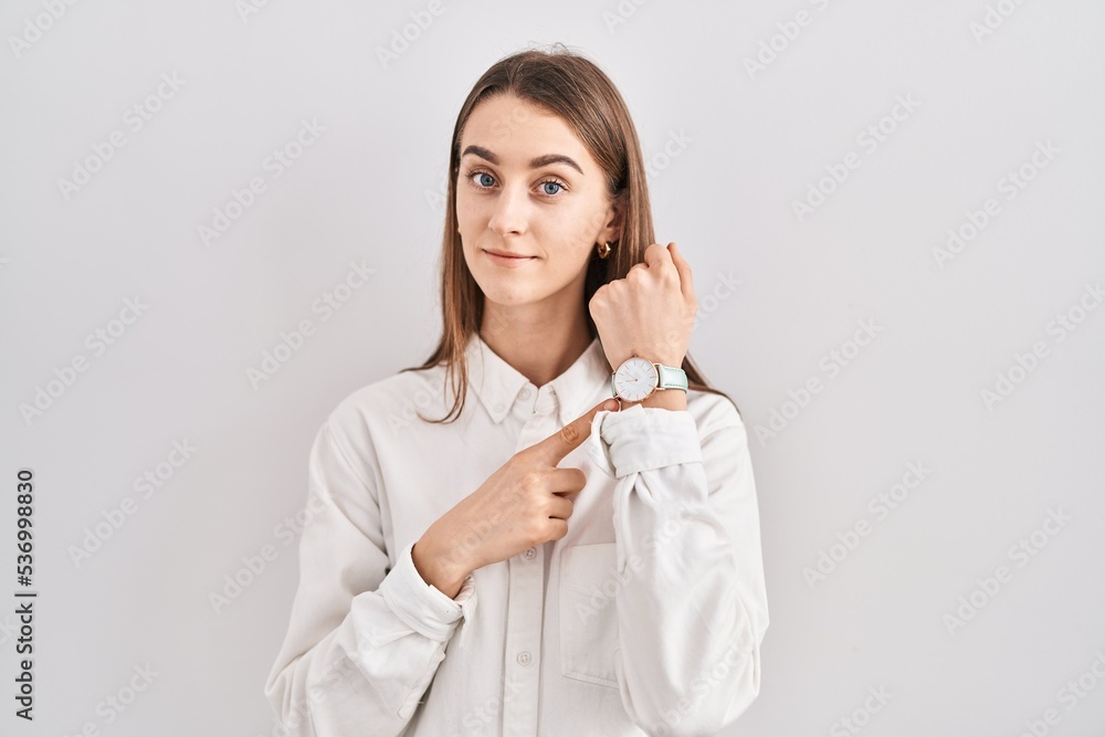 Young caucasian woman standing over isolated background in hurry pointing to watch time, impatience, looking at the camera with relaxed expression Young caucasian woman standing over isolated background in hurry pointing to watch time, impatience, looking at the camera with relaxed expression