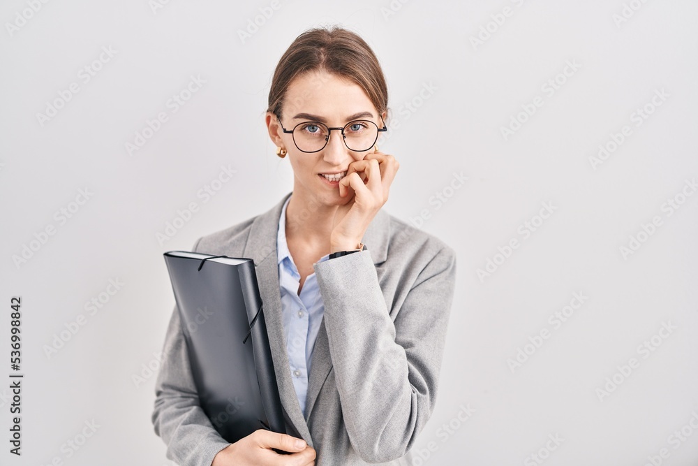 Young caucasian woman wearing business clothes and glasses looking stressed and nervous with hands on mouth biting nails. anxiety problem. Young caucasian woman wearing business clothes and glasses looking stressed and nervous with hands on mouth biting nails. anxiety problem.