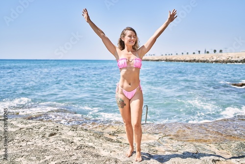 Young blonde girl wearing bikini with hands raised up at the beach.