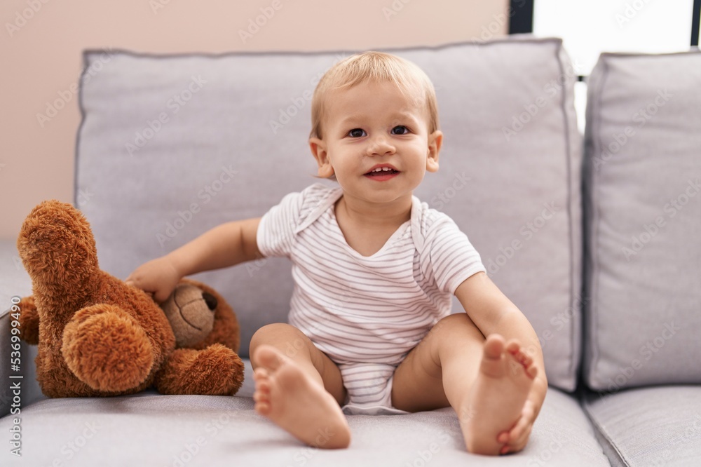 Adorable toddler playing with teddy bear sitting on sofa at home Adorable toddler playing with teddy bear sitting on sofa at home