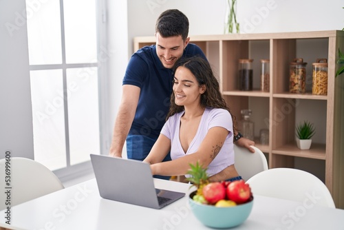 Young hispanic couple using laptop sitting on table at home