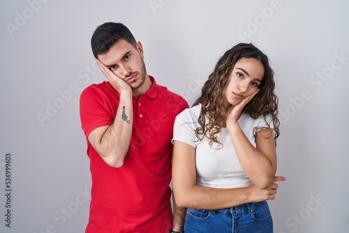 Young hispanic couple standing over isolated background thinking looking tired and bored with depression problems with crossed arms.