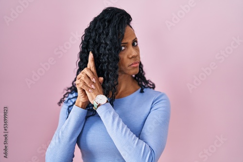 Middle age hispanic woman standing over pink background holding symbolic gun with hand gesture, playing killing shooting weapons, angry face