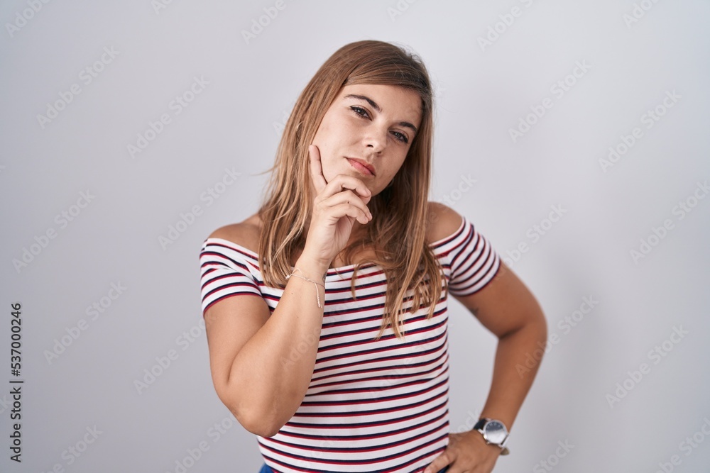 Young hispanic woman standing over isolated background with hand on chin thinking about question, pensive expression. smiling with thoughtful face. doubt concept. Young hispanic woman standing over isolated background with hand on chin thinking about question, pensive expression. smiling with thoughtful face. doubt concept.