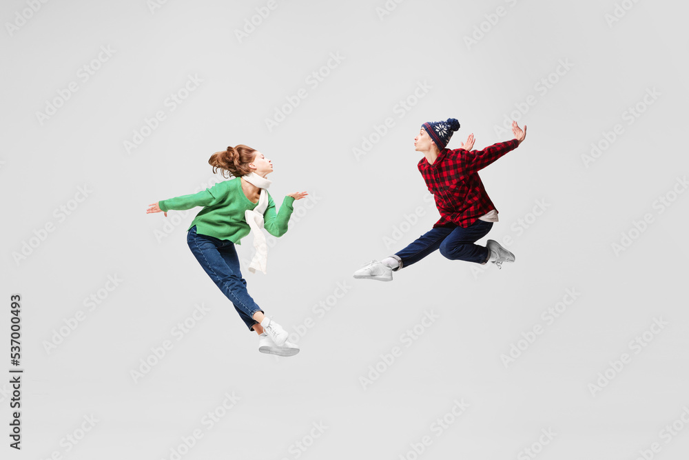 Creative portrait of ballet dancers in warm clothes and hats dancing, having fun isolated on gray background. Music, dance, fashion