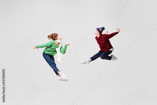 Creative portrait of ballet dancers in warm clothes and hats dancing, having fun isolated on gray background. Music, dance, fashion
