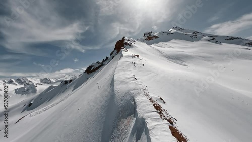 Aerial view flying over picturesque mountain ridge snowy rock texture sun light blue sky landscape. FPV sports drone empty alpine scenery winter glacier freeze valley natural cliff range freeze summit photo