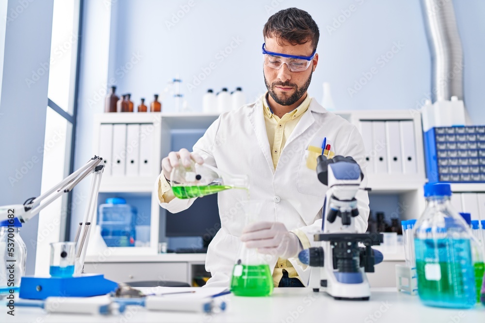 Young hispanic man wearing scientist uniform measuring liquid at laboratory Young hispanic man wearing scientist uniform measuring liquid at laboratory