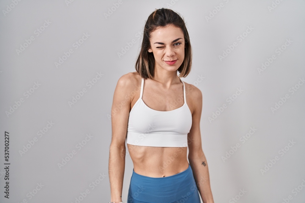 Hispanic woman wearing sportswear over isolated background winking looking at the camera with sexy expression, cheerful and happy face. Hispanic woman wearing sportswear over isolated background winking looking at the camera with sexy expression, cheerful and happy face.