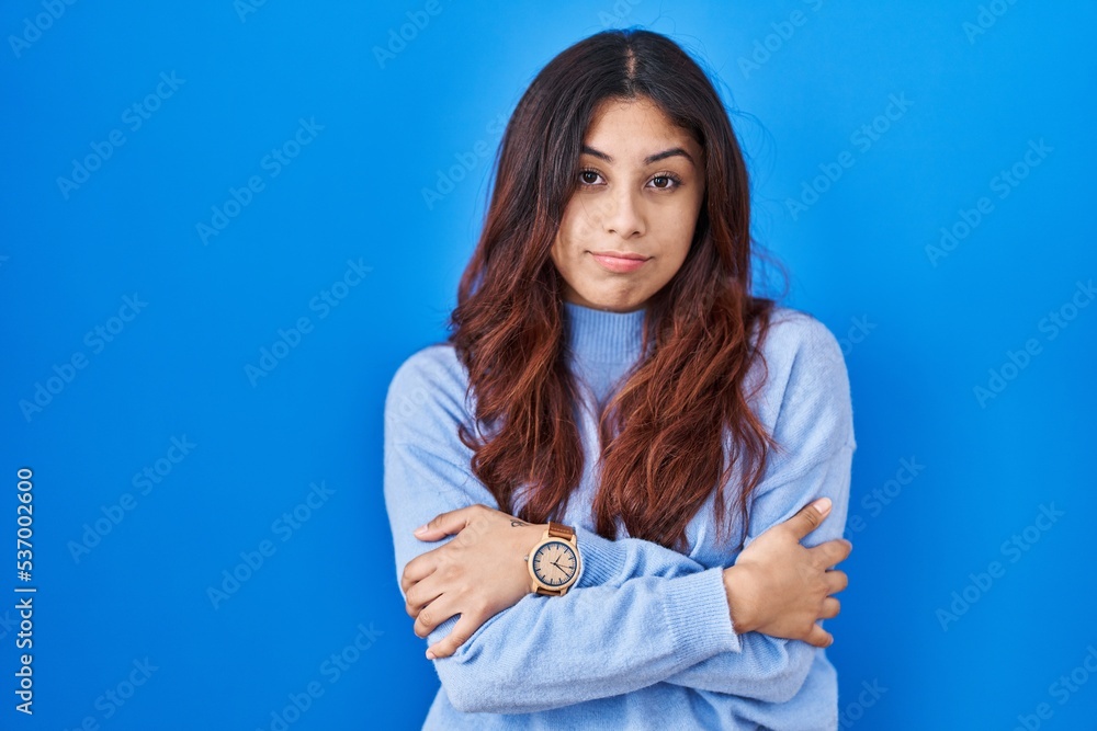 Hispanic young woman standing over blue background shaking and freezing for winter cold with sad and shock expression on face Hispanic young woman standing over blue background shaking and freezing for winter cold with sad and shock expression on face
