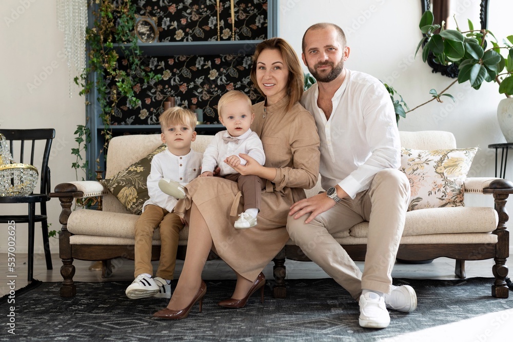 Happy family of mom dad and 2 little sons sitting on the sofa In beige clothes Happy family of mom dad and 2 little sons sitting on the sofa In beige clothes
