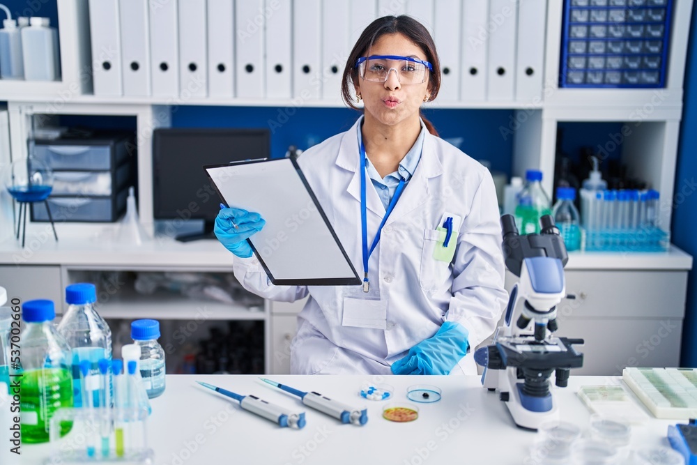 Hispanic young woman working at scientist laboratory looking at the camera blowing a kiss on air being lovely and sexy. love expression. Hispanic young woman working at scientist laboratory looking at the camera blowing a kiss on air being lovely and sexy. love expression.