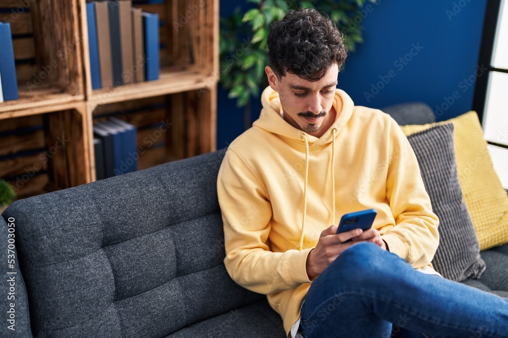 Young caucasian man using smartphone sitting on sofa at home Young caucasian man using smartphone sitting on sofa at home
