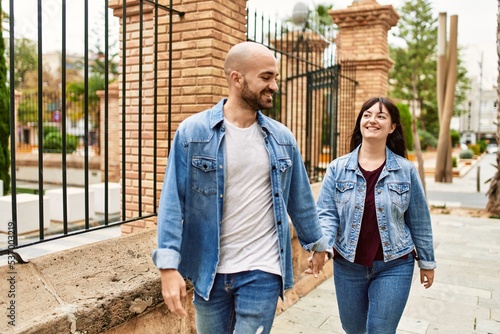 Young hispanic couple smiling happy walking with hands together at the city.