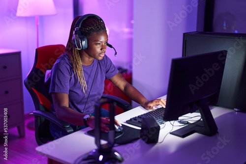 African american woman streamer playing video game using computer at gaming room