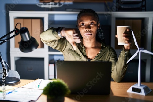 African woman working using computer laptop at night looking unhappy and angry showing rejection and negative with thumbs down gesture. bad expression.