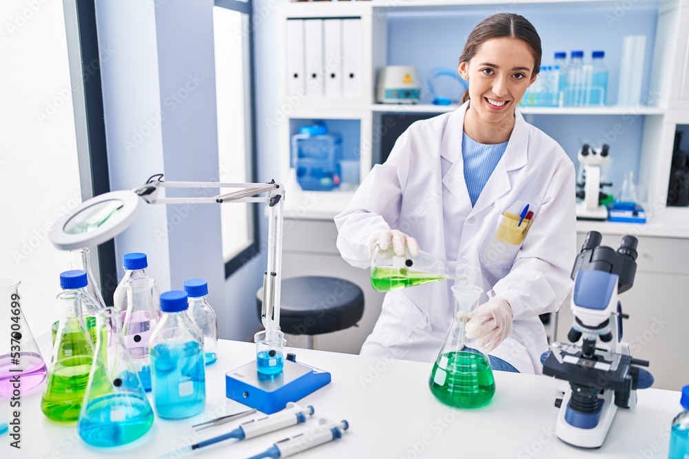 Young beautiful hispanic woman scientist pouring liquid on test tube at laboratory Young beautiful hispanic woman scientist pouring liquid on test tube at laboratory