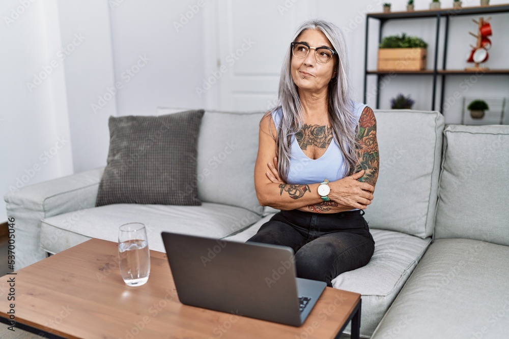 Middle age grey-haired woman using laptop at home smiling looking to the side and staring away thinking. Middle age grey-haired woman using laptop at home smiling looking to the side and staring away thinking.