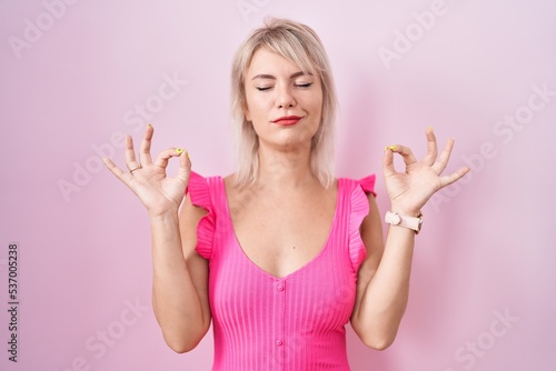 Young caucasian woman standing over pink background relaxed and smiling with eyes closed doing meditation gesture with fingers. yoga concept.