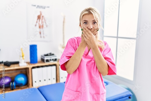 Young caucasian woman working at pain recovery clinic shocked covering mouth with hands for mistake. secret concept.