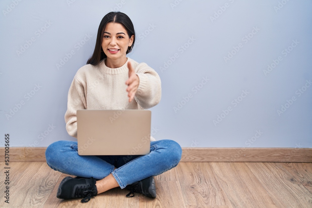 Young woman using laptop sitting on the floor at home smiling friendly offering handshake as greeting and welcoming. successful business. Young woman using laptop sitting on the floor at home smiling friendly offering handshake as greeting and welcoming. successful business.