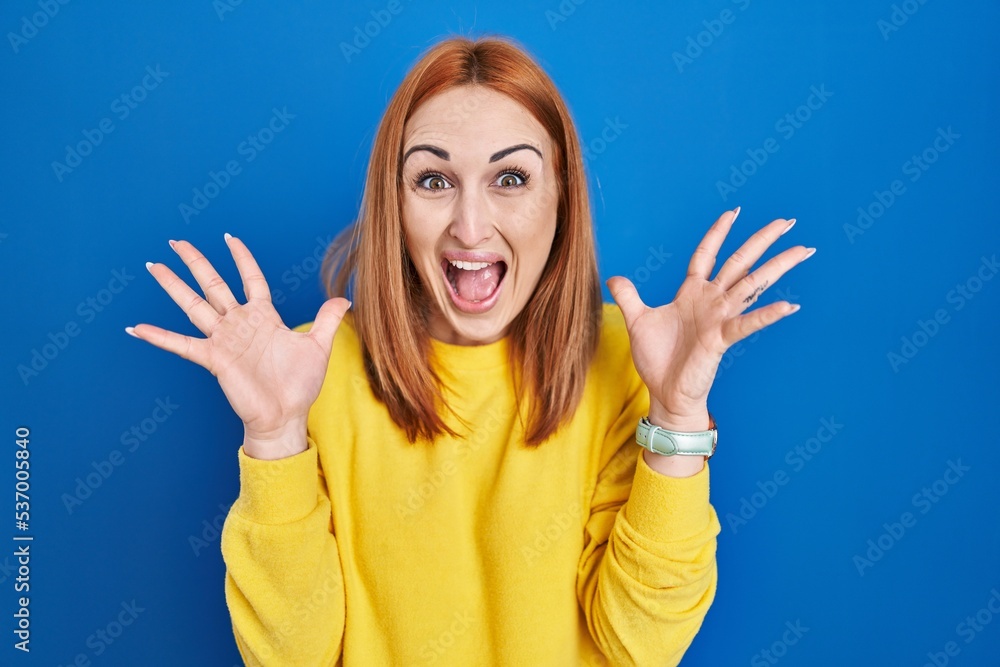Young woman standing over blue background celebrating crazy and amazed for success with arms raised and open eyes screaming excited. winner concept Young woman standing over blue background celebrating crazy and amazed for success with arms raised and open eyes screaming excited. winner concept