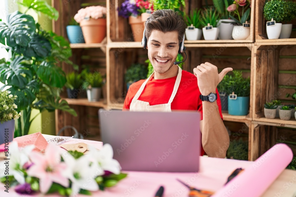 Fototapeta premium Young hispanic man working at florist shop doing video call pointing thumb up to the side smiling happy with open mouth