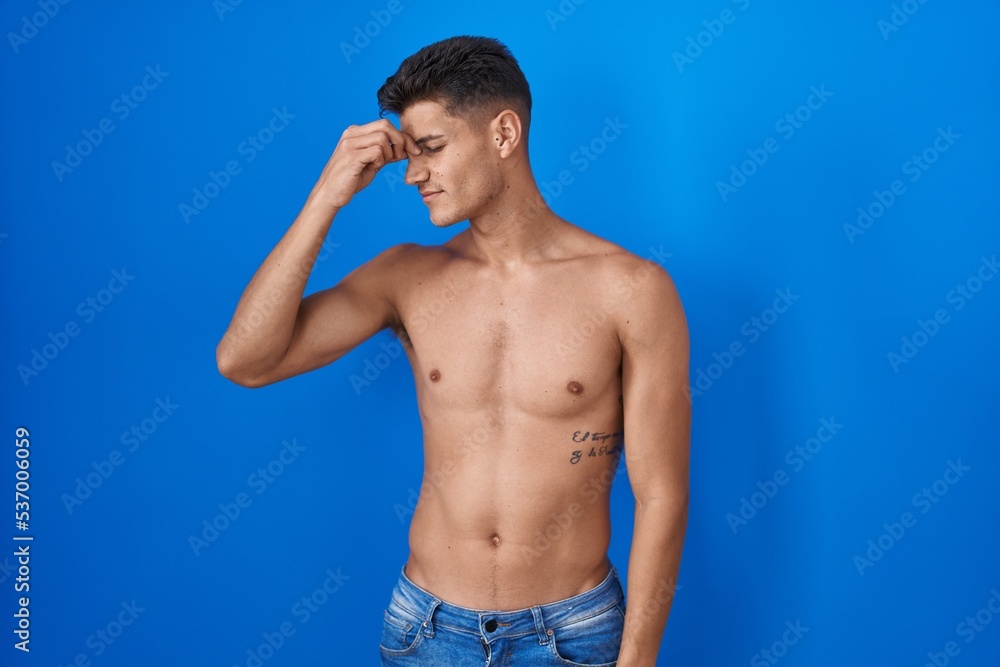 Naklejka premium Young hispanic man standing shirtless over blue background tired rubbing nose and eyes feeling fatigue and headache. stress and frustration concept.