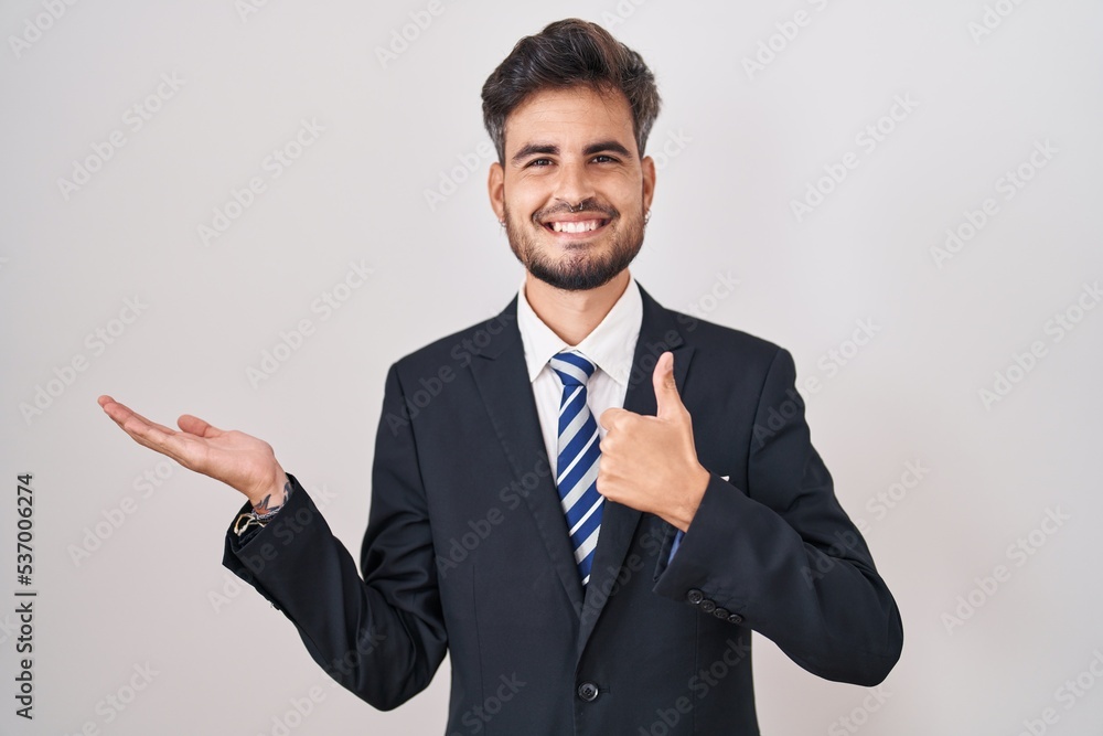 Young hispanic man with tattoos wearing business suit and tie showing palm hand and doing ok gesture with thumbs up, smiling happy and cheerful Young hispanic man with tattoos wearing business suit and tie showing palm hand and doing ok gesture with thumbs up, smiling happy and cheerful