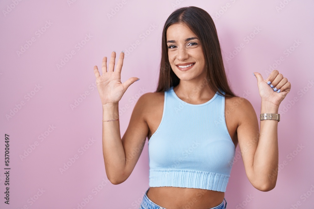 Young brunette woman standing over pink background showing and pointing up with fingers number six while smiling confident and happy.