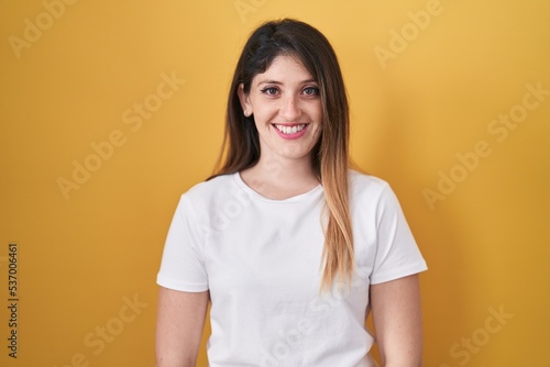 Young brunette woman standing over yellow background with a happy and cool smile on face. lucky person.