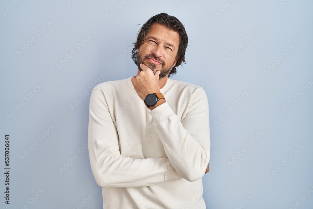 Handsome middle age man wearing casual sweater over blue background looking confident at the camera with smile with crossed arms and hand raised on chin. thinking positive. Handsome middle age man wearing casual sweater over blue background looking confident at the camera with smile with crossed arms and hand raised on chin. thinking positive.