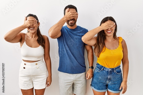 Group of young hispanic people standing over isolated background smiling and laughing with hand on face covering eyes for surprise. blind concept.