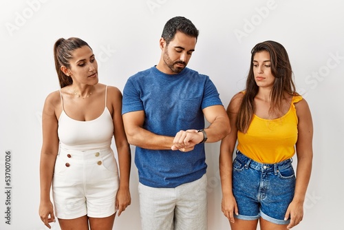 Group of young hispanic people standing over isolated background checking the time on wrist watch  relaxed and confident