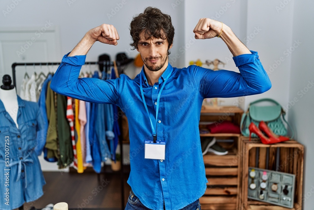 Young hispanic man working as manager at retail boutique showing arms muscles smiling proud. fitness concept. Young hispanic man working as manager at retail boutique showing arms muscles smiling proud. fitness concept.