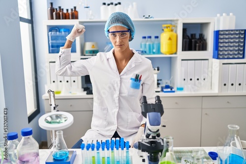 Brunette woman working at scientist laboratory strong person showing arm muscle, confident and proud of power