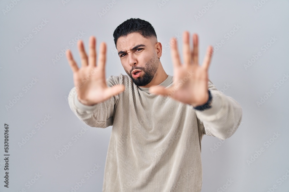 Fototapeta premium Young handsome man standing over isolated background afraid and terrified with fear expression stop gesture with hands, shouting in shock. panic concept.