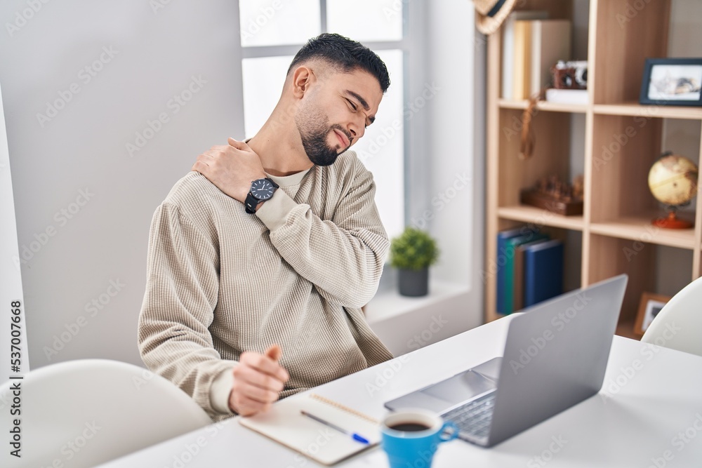 Naklejka premium Young arab man suffering for back ache sitting on table working at home