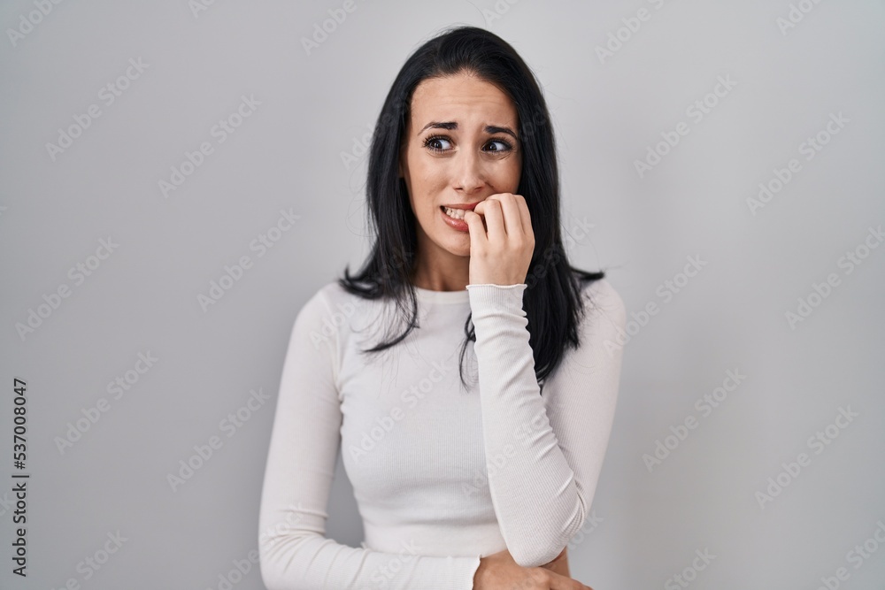 Hispanic woman standing over isolated background looking stressed and nervous with hands on mouth biting nails. anxiety problem. Hispanic woman standing over isolated background looking stressed and nervous with hands on mouth biting nails. anxiety problem.