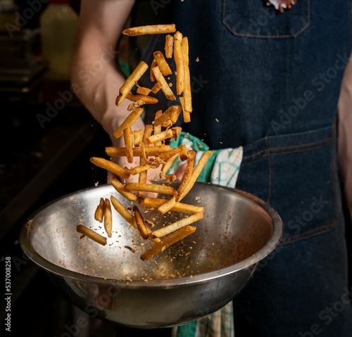 Fotografie Person tossing freshly cooked fries with spices on a mixing bowl