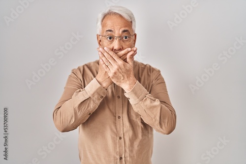 Hispanic senior man wearing glasses shocked covering mouth with hands for mistake. secret concept. © Krakenimages.com