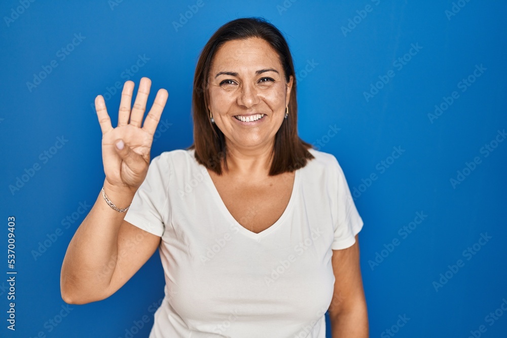 Hispanic mature woman standing over blue background showing and pointing up with fingers number four while smiling confident and happy. Hispanic mature woman standing over blue background showing and pointing up with fingers number four while smiling confident and happy.