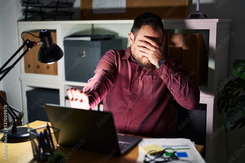 Plus size hispanic man with beard working at the office at night covering eyes with hands and doing stop gesture with sad and fear expression. embarrassed and negative concept. Plus size hispanic man with beard working at the office at night covering eyes with hands and doing stop gesture with sad and fear expression. embarrassed and negative concept.