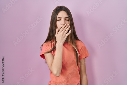Teenager girl standing over pink background bored yawning tired covering mouth with hand. restless and sleepiness.