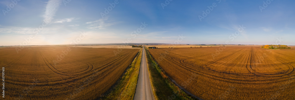 Aerial view looking down a country road surrounded by harvested grain fields under a blue sky with wispy white clouds
