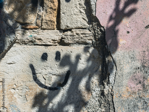 Old stone wall with smiley face graffiti and shadows  