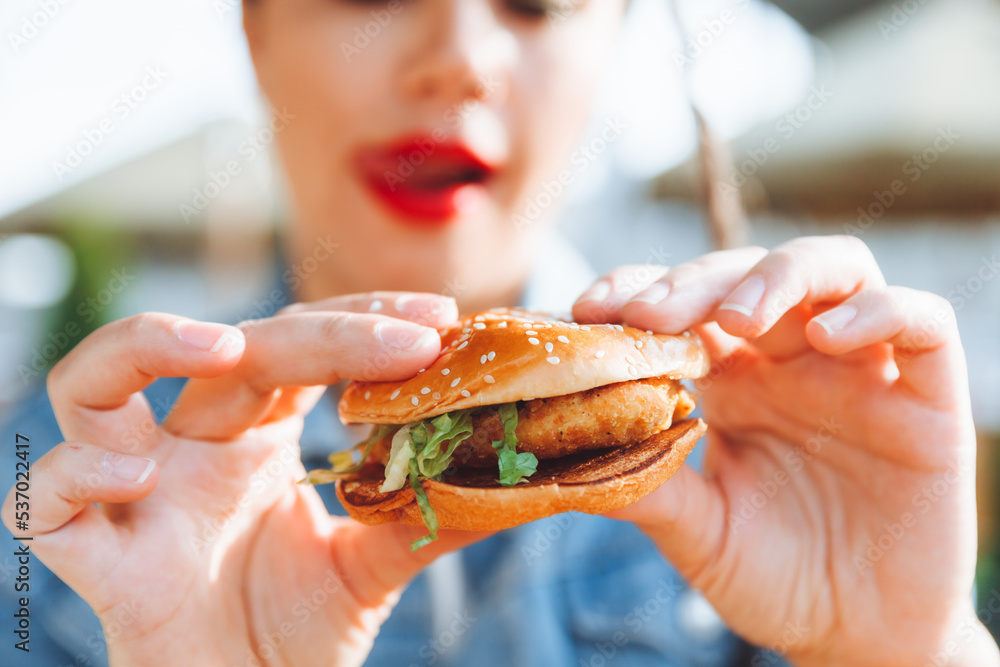 A young glamorous woman with dreadlocks and red lipstick is sitting and eating a burger in a street cafe, the concept of eating. long-lasting lipstick A young glamorous woman with dreadlocks and red lipstick is sitting and eating a burger in a street cafe, the concept of eating. long-lasting lipstick