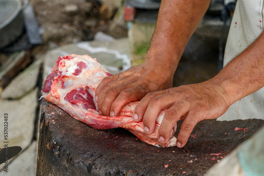 Men in the countryside cut up pieces of beef. The farmer is holding a piece of meat.