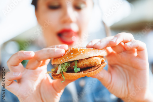 A young glamorous woman with dreadlocks and red lipstick is sitting and eating a burger in a street cafe, the concept of eating. long-lasting lipstick